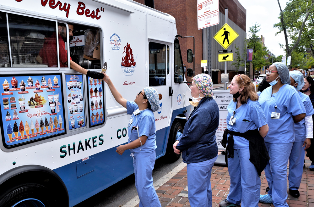 A group of Penn Medicine employees wearing blue scrubs form a line in front of an ice cream truck.